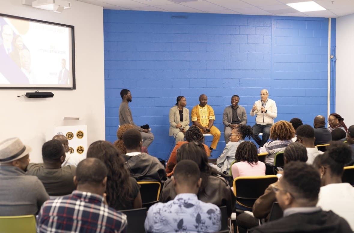 Wide view of the room during the talk, with the panel in front of a blue wall